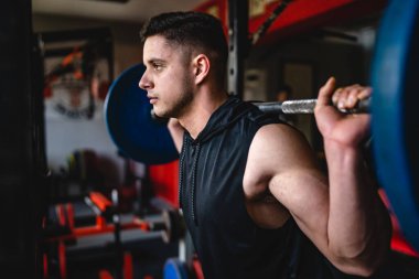 Spor salonundaki erkek sporcu, amatör ya da sporcu halterli ve omuzlarında ağırlık olan biri fotokopi alanı dayanıklılığını ve vücut geliştirme konseptini kapatıyor.