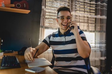 Kafkasyalı mutlu bir genç adam telefon görüşmesi yapıyor ve gülümsüyor. Elinde not defteri ve hesap makinesiyle evdeki masada otururken iyi bir haber kavramı var.
