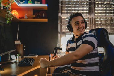 Kafasında kulaklıklarla evde tek başına bilgisayar başında video oyunu oynayan beyaz bir erkek. Mutlu, gülümseyen gerçek insanlar uzayı kopyalıyor.