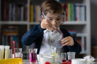 Beş yaşında, koruyucu gözlüklü beyaz bir bilim adamı masada oturmuş kimya ekipmanları oyuncaklarıyla oynuyor deney öncesi öğrenme ve eğitim konsepti ön görüşüyle oynuyor.