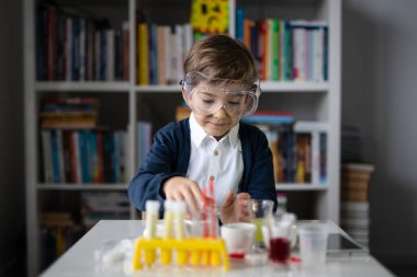 Beş yaşında, koruyucu gözlüklü beyaz bir bilim adamı masada oturmuş kimya ekipmanları oyuncaklarıyla oynuyor deney öncesi öğrenme ve eğitim konsepti ön görüşüyle oynuyor.