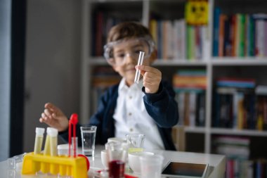 Beş yaşında, koruyucu gözlüklü beyaz bir bilim adamı masada oturmuş kimya ekipmanları oyuncaklarıyla oynuyor deney öncesi öğrenme ve eğitim konsepti ön görüşüyle oynuyor.