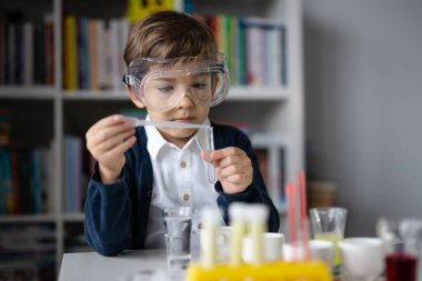 Beş yaşında, koruyucu gözlüklü beyaz bir bilim adamı masada oturmuş kimya ekipmanları oyuncaklarıyla oynuyor deney öncesi öğrenme ve eğitim konsepti ön görüşüyle oynuyor.