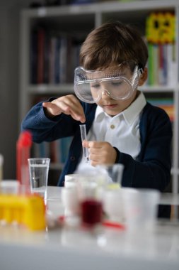 Beş yaşında, koruyucu gözlüklü beyaz bir bilim adamı masada oturmuş kimya ekipmanları oyuncaklarıyla oynuyor deney öncesi öğrenme ve eğitim konsepti ön görüşüyle oynuyor.