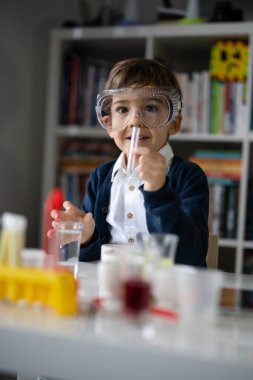 Beş yaşında, koruyucu gözlüklü beyaz bir bilim adamı masada oturmuş kimya ekipmanları oyuncaklarıyla oynuyor deney öncesi öğrenme ve eğitim konsepti ön görüşüyle oynuyor.