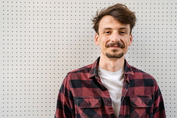 One young caucasian man with brown hair and mustaches wearing shirt looking to the camera modern happy adult male smile portrait in front of white wall copy space close up