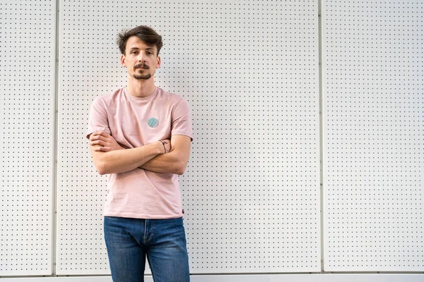 One young caucasian man with brown hair and mustaches wearing t-shirt looking to the camera modern serious adult male portrait in front of white wall copy space waist up