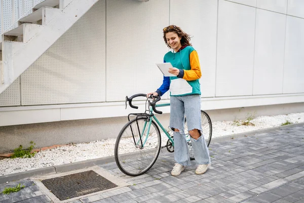 一人の女性若い大人の白人女性が歩いて大学の建物を保持自転車やデジタルタブレットで一日本物の人々はスペースをコピーフル長辺のビュー — ストック写真