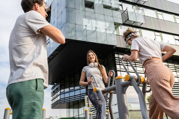 Bir grup arkadaş, erkek ve kadın, erkek ve genç, açık havada spor salonunda, modern binanın önünde antrenman yapıyorlar. Gerçek insanlar spor ve eğlence, sağlıklı yaşam tarzı kavramları geliştiriyorlar.