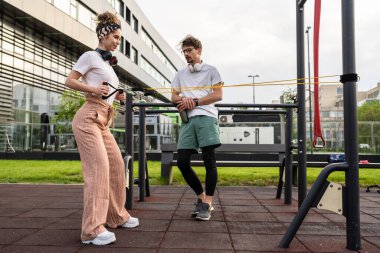 Kafkasyalı genç bir çift erkek ve kadın erkek arkadaş veya karı koca açık spor salonunda eğitim görüyor elastik direnç bandı tüpleri fotokopi alanında egzersiz yapıyorlar.
