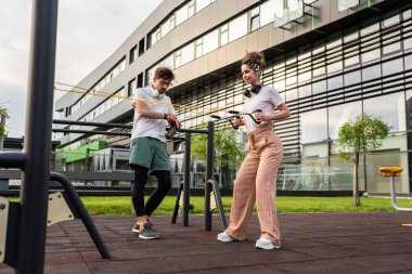 Kafkasyalı genç bir çift erkek ve kadın erkek arkadaş veya karı koca açık spor salonunda eğitim görüyor elastik direnç bandı tüpleri fotokopi alanında egzersiz yapıyorlar.
