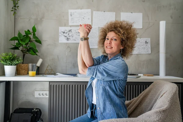 One woman adult mature caucasian female at her office desk sitting at work stretching arms Relaxation exercise Resting while taking a brake Workplace Concept copy space real people