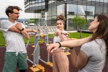 Bir grup arkadaş şehirdeki açık spor salonunda antrenmandan önce ya da sonra esneme hareketleri yapan kadın ve erkek. Gerçek insanlar sağlıklı yaşam tarzı konsepti, amatörler spor yapıyor.