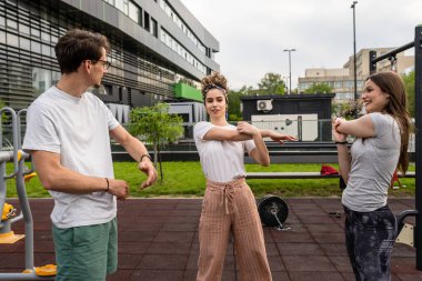 Bir grup arkadaş şehirdeki açık spor salonunda antrenmandan önce ya da sonra esneme hareketleri yapan kadın ve erkek. Gerçek insanlar sağlıklı yaşam tarzı konsepti, amatörler spor yapıyor.