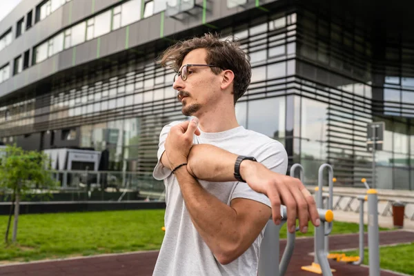 One man stretch arm before training while standing at open gym in the city