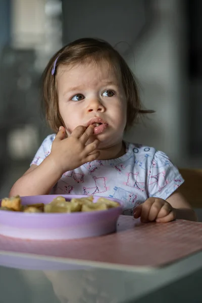 一人で家のテーブルに座っている一人の女の子の小さな白人の子供は 一日に一人で朝食やランチの食事のペストリーを食べます開発コンセプトコピースペースを成長現実の人々 — ストック写真
