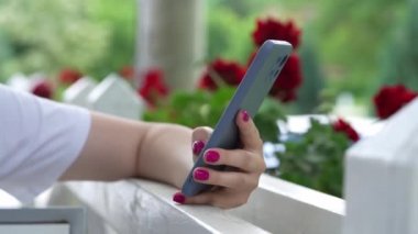Açık havada otururken, mesaj atmak ve iletişim kurmak için cep telefonu kullanan kimliği belirsiz beyaz kadının ellerini kapatın. 