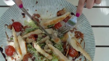 Kimliği belirsiz beyaz bir kadının tabaktan yemek yemek yemek için çatal ve bıçak kullanışının üst görüntüsü.