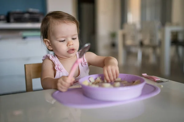 1人の子供小さな白人の幼児女性の赤ちゃんがテーブルで一人で家で食べる現実の人々はスペースをコピー初期の子供の発達コンセプトサイドビューは 食品を保持健康的な食事を保持 — ストック写真
