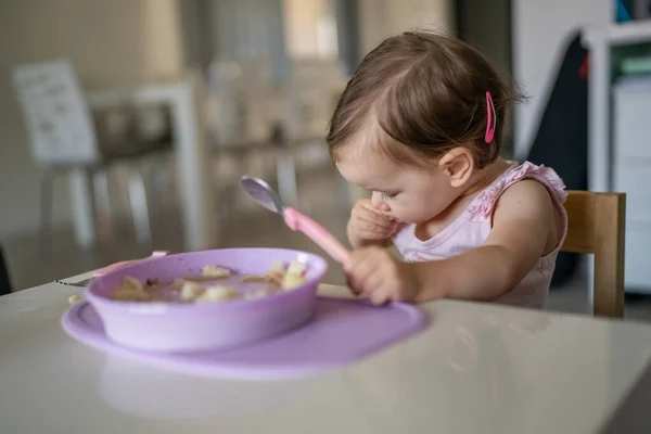 1人の子供小さな白人の幼児女性の赤ちゃんは 部屋の自宅で一人でテーブルで食べるスプーンを保持します — ストック写真