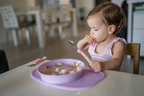 1人の子供小さな白人の幼児女性の赤ちゃんは 部屋の自宅で一人でテーブルで食べるスプーンを保持します — ストック写真