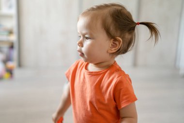one girl front view portrait of beautiful small caucasian toddler walking or standing at home alone while play wearing orange shirt growing up childhood and development concept copy space