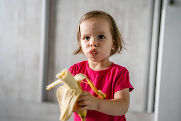 One Small Caucasian Girl Little Toddler Child Eating Banana Home — Stock Photo, Image