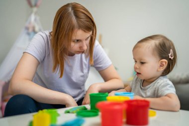 One girl small caucasian toddler child playing with colorful plasticine on the table at home with her mother woman childhood and growing up development concept copy space