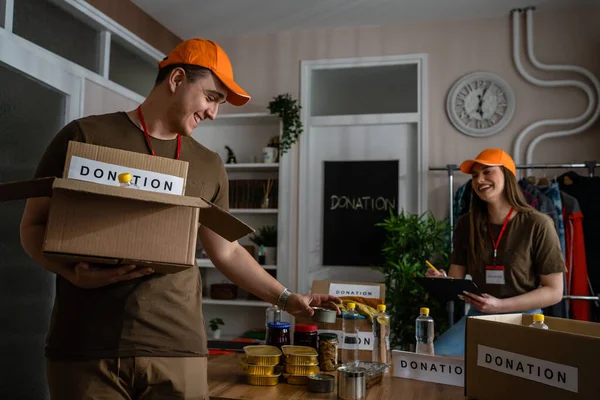两名男女志愿者准备捐款给慈善机构快乐志愿者在慈善基金会工作分离整理东西把食物和衣服放进盒子 — 图库照片