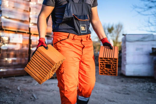 Güneşli yaz günlerinde turuncu içi boş kil blokları alan inşaat işçisinin elleri ve göbeğine yakın durun.