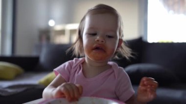 one girl small caucasian toddler female child daughter eating alone at the table at home while watching tv making mess on her face dirty sauce childhood growing up development concept copy space