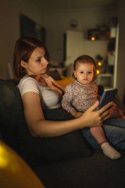 Küçük beyaz çocuk küçük kız bebek anne ve kız geceleri karanlık bir odada kanepede oturur çizgi film veya film izlerler cep telefonunda gerçek aile fotokopi çekerek büyürler.