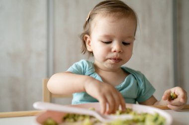 Bir küçük beyaz çocuk evde masada tek başına oturmuş plastik çatal kullanarak yemek yiyor. Çocukluk çağında ve gelişim konseptinde fotokopi uzayı sağlıklı yiyor.