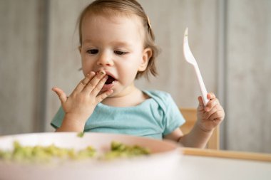 Bir küçük beyaz çocuk evde masada tek başına oturmuş plastik çatal kullanarak yemek yiyor. Çocukluk çağında ve gelişim konseptinde fotokopi uzayı sağlıklı yiyor.