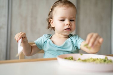 Bir küçük beyaz çocuk evde masada tek başına oturmuş plastik çatal kullanarak yemek yiyor. Çocukluk çağında ve gelişim konseptinde fotokopi uzayı sağlıklı yiyor.