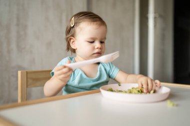 Bir küçük beyaz çocuk evde masada tek başına oturmuş plastik çatal kullanarak yemek yiyor. Çocukluk çağında ve gelişim konseptinde fotokopi uzayı sağlıklı yiyor.