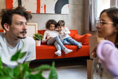 Çocuklar cep telefonuyla video oyunu oynarken ebeveynler kişisel eşyalarını alıp yeni bir daireye taşınıyorlar. Gerçek insanlar, beyaz erkek ve kadın kardeşlerini taklit ediyorlar.