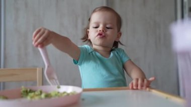 Bir küçük beyaz çocuk evde masada tek başına oturmuş plastik çatal kullanarak yemek yiyor. Çocukluk çağında ve gelişim konseptinde fotokopi uzayı sağlıklı yiyor.