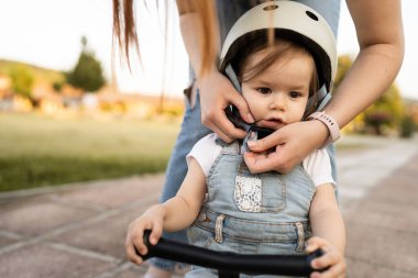 Küçük beyaz bir kız ya da erkek anne. Genç bir kadın koruyucu kaskı takıyor. Kızını çocuk kaskı takıyor.