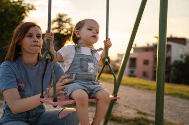 Küçük kız, annesiyle parkta gezerken güneşli bir günde eğlenirken çocuğunun sallanmasına yardım ediyor. Aile büyüyüp konsept uzay fotokopisi çekiyor.