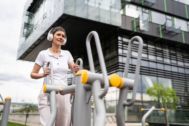 Gündüz bina önünde kısa saç eğitimi alan modern, olgun bir kadın spor salonunda eliptik eğitim makinesi simülatöründe sağlıklı yaşam tarzı konsepti sunuyor.