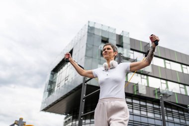 Bir kadın olgun ya da yaşlı, kauçuk elastik direnç bantlı beyaz kadın eğitimi. Açık spor salonunun spor salonundaki tüplerde. Sağlıklı yaşam tarzı konsepti.