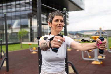 Bir kadın olgun ya da yaşlı, kauçuk elastik direnç bantlı beyaz kadın eğitimi. Açık spor salonunun spor salonundaki tüplerde. Sağlıklı yaşam tarzı konsepti.