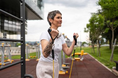 Bir kadın olgun ya da yaşlı, kauçuk elastik direnç bantlı beyaz kadın eğitimi. Açık spor salonunun spor salonundaki tüplerde. Sağlıklı yaşam tarzı konsepti.