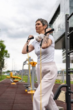 Bir kadın olgun ya da yaşlı, kauçuk elastik direnç bantlı beyaz kadın eğitimi. Açık spor salonunun spor salonundaki tüplerde. Sağlıklı yaşam tarzı konsepti.
