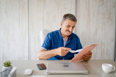 one senior man male caucasian entrepreneur or businessman checking documents or contract or report while sitting at the table desk in the office alone happy confident real people copy space