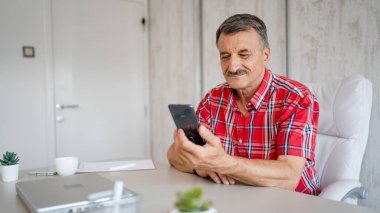 Üst düzey bir erkek girişimci iş yerindeki masada oturuyor bir fincan kahve ve cep telefonu tutuyor online mesajları veya sosyal medya içeriğini kontrol ediyor gerçek insanlar boşluğu kopyalıyor