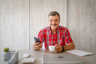 Üst düzey bir erkek girişimci iş yerindeki masada oturuyor bir fincan kahve ve cep telefonu tutuyor online mesajları veya sosyal medya içeriğini kontrol ediyor gerçek insanlar boşluğu kopyalıyor