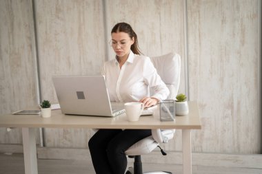 One woman female caucasian entrepreneur businesswoman or secretary sitting at her office at desk work on laptop computer happy smile wear white shirt copy space
