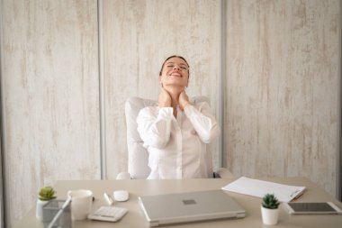 Bir kadın beyaz girişimci iş kadını ya da sekreter, iş yerinde, boynu tutulmuş, ağrılı bir şekilde masada oturuyor. Acılı omzuna sarılmış, rahatlamaya çalışıyor.